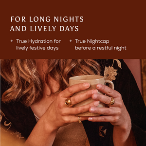 A person with gold rings on their hands holds a ceramic mug of Ancient + Brave Revelry + Rest Cracker for festive electrolyte replenishment and restorative sleep.