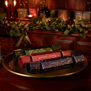 Ancient + Brave Wellness Christmas Cracker Set featuring three crackers in green, red, and blue resting on a gold platter.