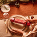 Hands holding an Ancient + Brave Radiance + Restore Cracker over a dinner plate at a table set with a cocktail glass and cutlery.