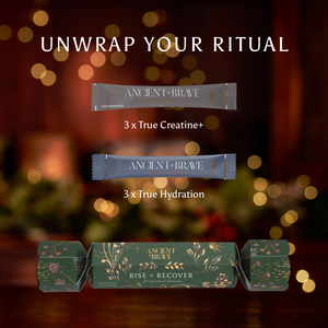 An Ancient + Brave Rise + Recover Cracker displayed with three sachets of True Creatine+, three sachets of True Hydration, and a green luxury wellbeing Christmas cracker decorated with gold foliage.