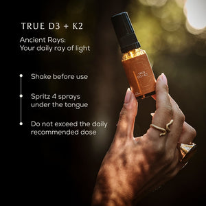 A hand holds a bottle from the Ancient + Brave True Vitamin D3 + K2 - 3 Pack, labeled as a vitamin D3 spray. The instructions read: shake before use and spritz 4 sprays under the tongue, without exceeding the daily recommended dose. Warm sunlight bathes the scene, emphasizing this supplement’s role in supporting bone health and overall wellness.