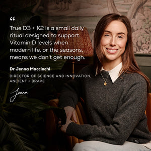 A woman sits on a green couch, smiling, with text beside her highlighting the bone support benefits of Ancient + Brave True Vitamin D3 + K2 – 3 Pack. The background features plants and framed artwork on the wall.