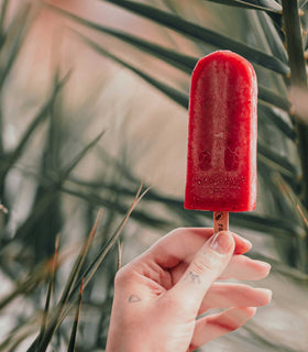 Red popsicle held by a hand against a blurred natural background