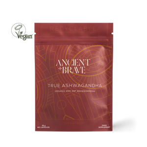 Ancient + Brave True Ashwagandha food supplement pouch in a deep reddish-brown color with gold geometric patterns, shown on a white background with a Vegan logo overlay.