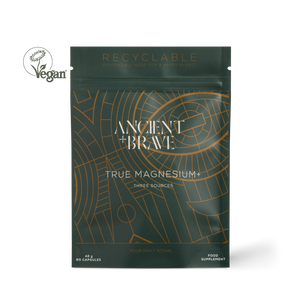 A dark green stand-up pouch of Ancient + Brave True Magnesium+ food supplement, featuring gold geometric line art and white text. A white 'Vegan' logo is visible in the top-left corner of the image.