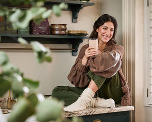 Woman holding a glass of Ancient + Brave's Protein in a kitchen setting