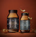 Two amber jars of collagen peptides and creatine supplements with gold labels from the Ancient + Brave Davina Ritual Gift Set, accompanied by a gold measuring scoop and gold ribbon.
