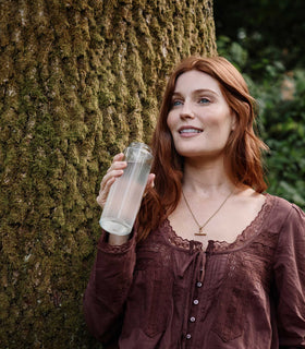 Woman holding a water bottle next to a tree in a natural setting
