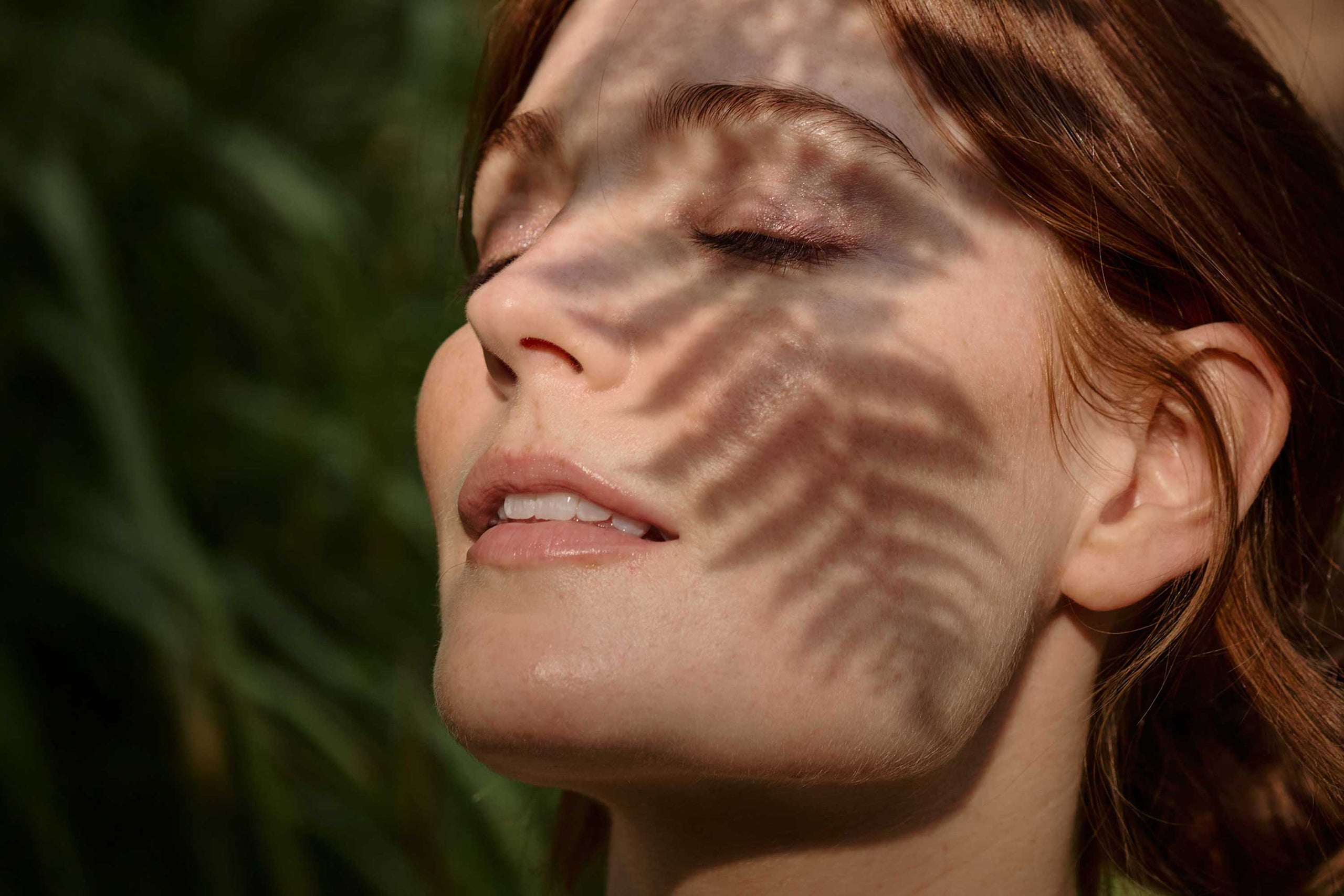 Close-up of a woman's face with sunlight casting shadows on her skin.