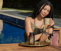 Woman holding a cup by a poolside with a bottle of Ancient + Brave's True Collagen and tray on a table