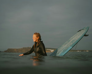 Person in a wetsuit holding a surfboard in the water with a dark, overcast sky.