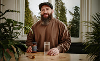 Joe Marler sitting at a table with a glass of water and a jar of True Hydration, surrounded by plants.