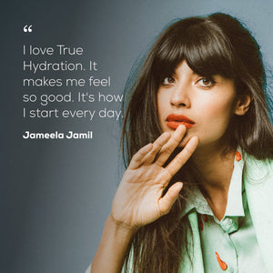 A portrait-style quote graphic featuring a woman with dark hair and bangs wearing a pale green collared shirt, with a gray background and white text that reads: “I love True Hydration. It makes me feel so good. It's how I start every day."