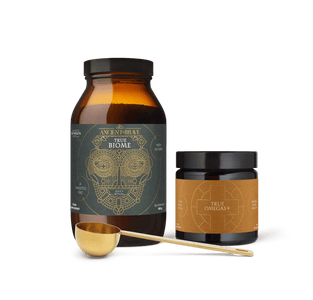 Two brown containers from Ancient + Brave’s Longevity Bundle, featuring gold and black labels, are displayed with a gold measuring scoop on a white background—expertly formulated to support gut health and provide essential fatty acids for long-term wellbeing.