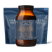 An amber glass jar of Ancient + Brave Wild Collagen centered in front of two blue resealable pouches on a black background.