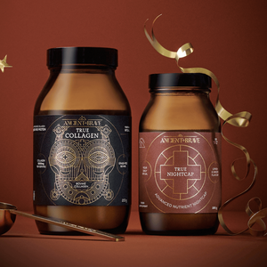 Two amber glass jars of Ancient + Brave Rest Gift Set collagen peptides with gold-foiled labels, accompanied by a gold measuring spoon and decorative gold ribbons.