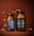 An Ancient + Brave Rise Gift Set consisting of two brown glass supplement jars of electrolyte powder and collagen peptides, decorated with a gold ribbon and a small star ornament.
