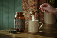 Jar of True Collagen with a mug next to it and a scoop of powder being poured into the drink