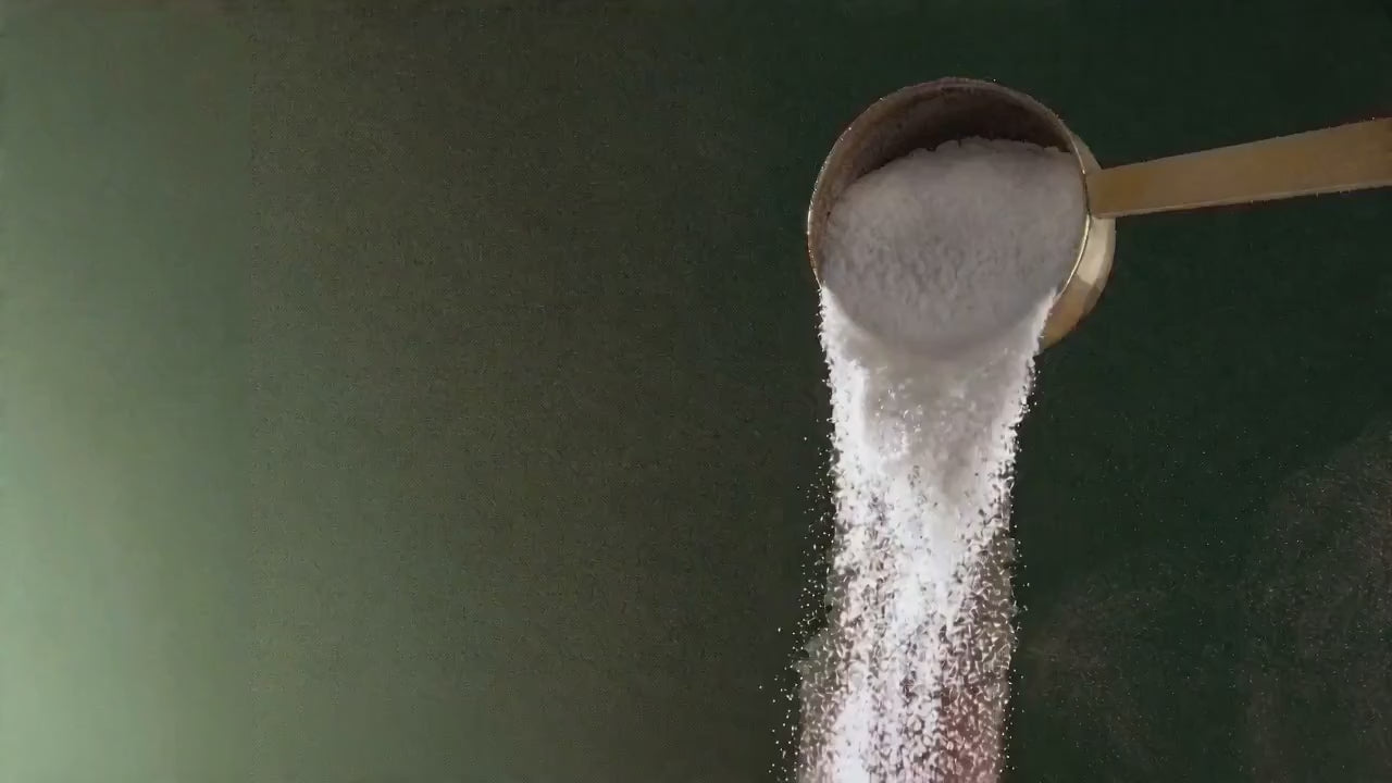 Collagen powder being poured from a scoop in slow motion on a green background