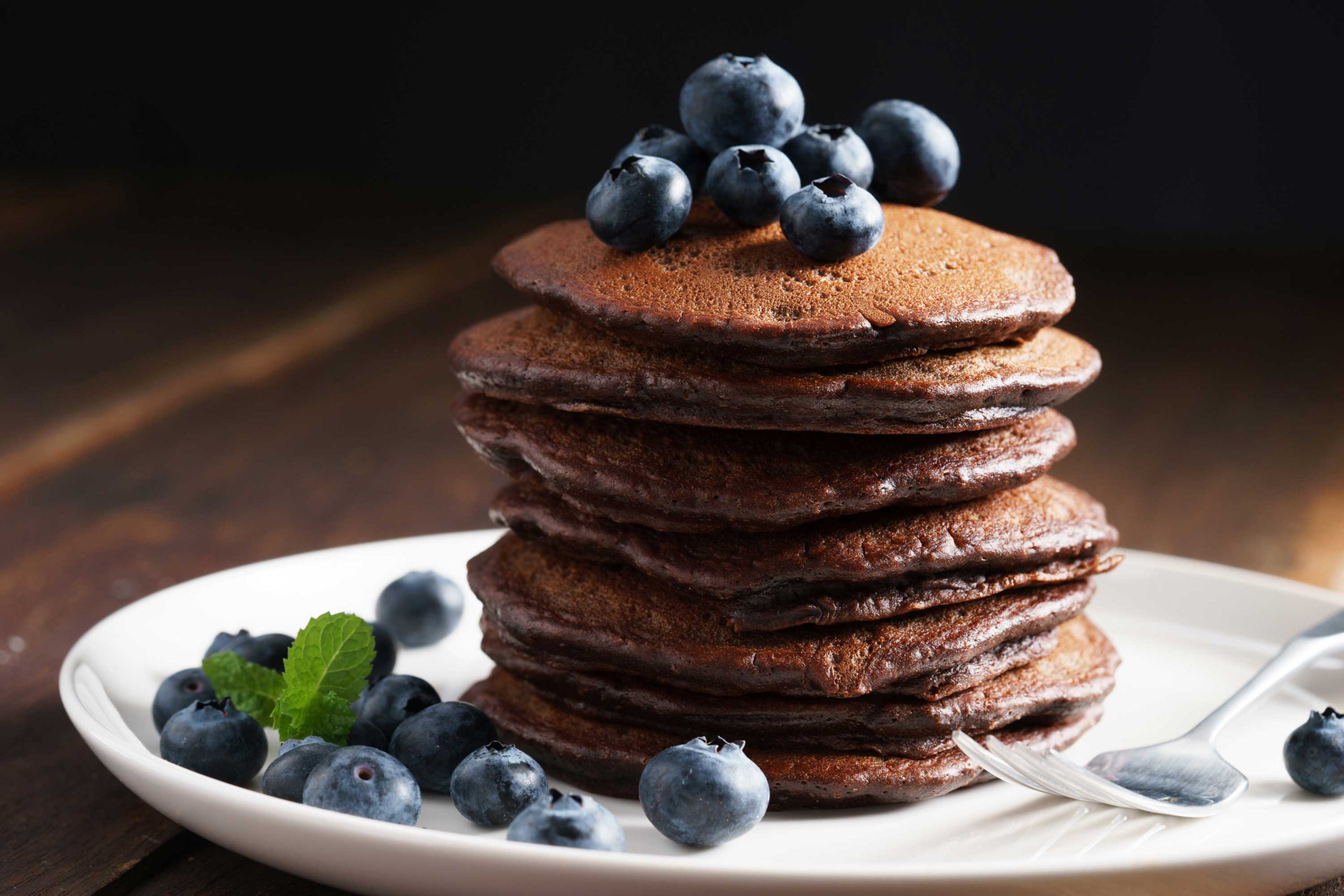 Stack of chocolate pancakes with blueberries on a white plate