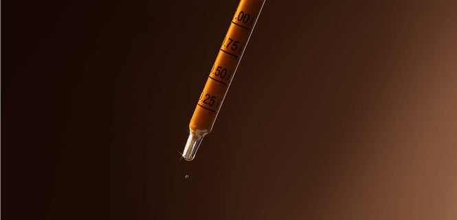 Dropper with liquid being dispensed on a dark background
